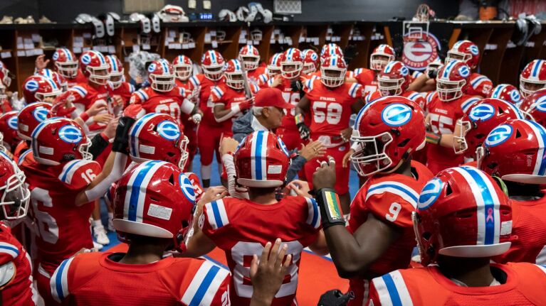 Football players in red uniforms gather for pre-game motivational moment.