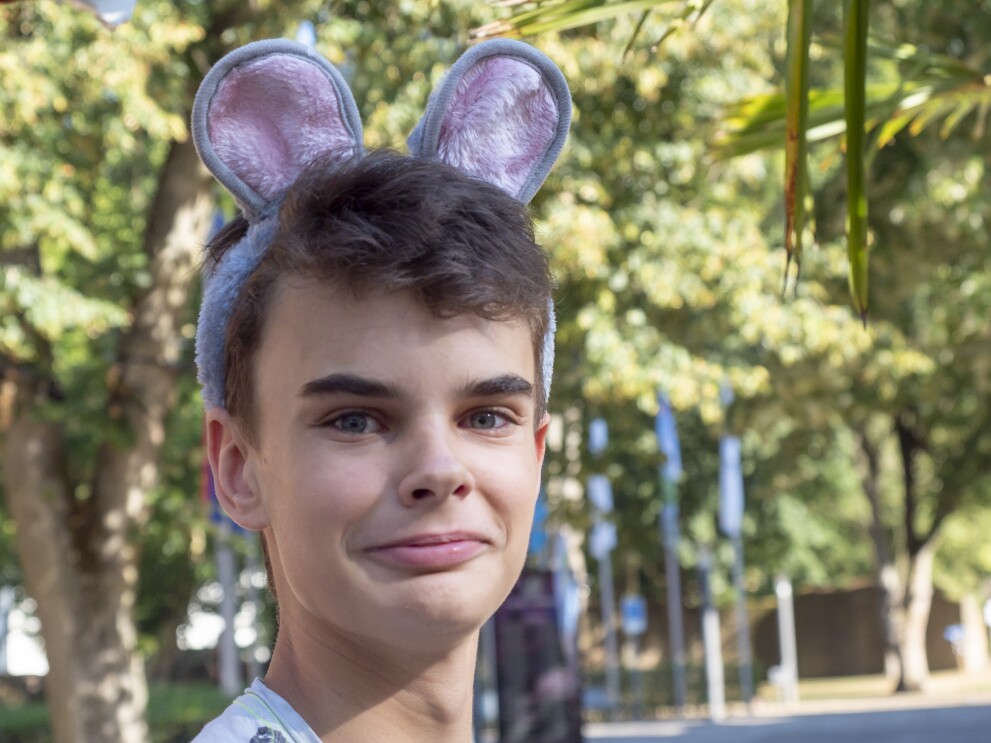 Die Poträtaufnahme zeigt einen Jungen von ca. 10 Jahren der Plüsch-Mäuseohren trägt. Er hat braune Augen, blickt direkt in die Kamera.