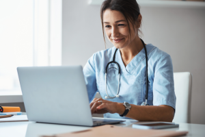 A doctor working on a laptop device at their desk in a clinic.