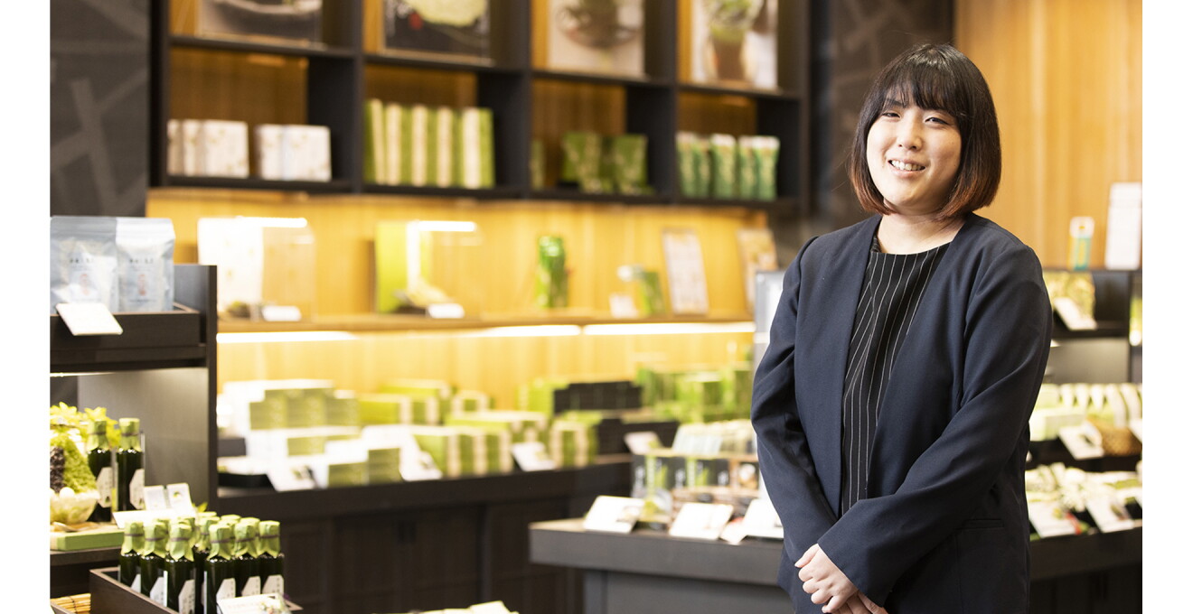 宇治茶・宇治抹茶製品が並ぶ店舗に立つ足立さん