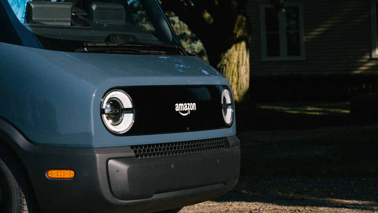 The front end of an electric delivery vehicle, showing headlights and the Amazon logo.