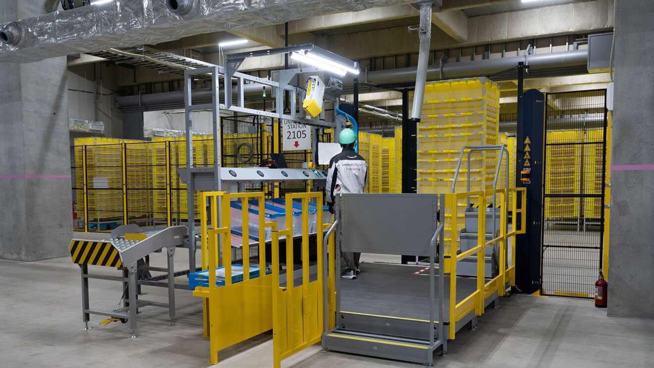 黒い金網のフェンスの手前に約2畳ほどの広さの作業スペースが設けられている。金網のフェンスの向こうにはARの黄色い棚が並んでいる