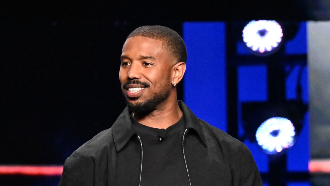 Michael B. Jordan smiling against blue backdrop with white circular lights.