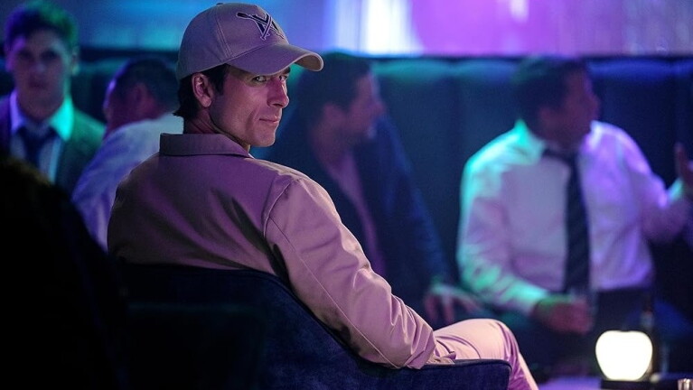 Man wearing a baseball cap, seated, looking toward the camera 