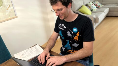 Cristian Perfumo, el escritor de la Patagonia, está sentado en una mesa de comedor y trabajando en su ordenador. Viste una camiseta deportiva y en la mesa tiene unas hojas de papel con correcciones en color rojo.