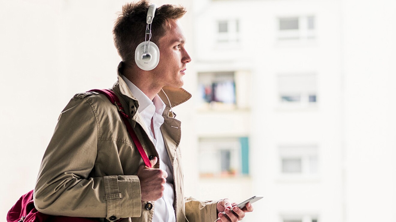 A stylishly dressed man listens to audio from his smartphone via headphones