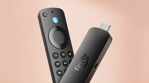 ベージュの背景に、黒い直方体のデバイスを2個V字形に重ねて配置。左側はリモコンで表面に複数のボタン、右側の表面にはfiretvのロゴ、先端にUSB差込口のような銀色の部分がある。