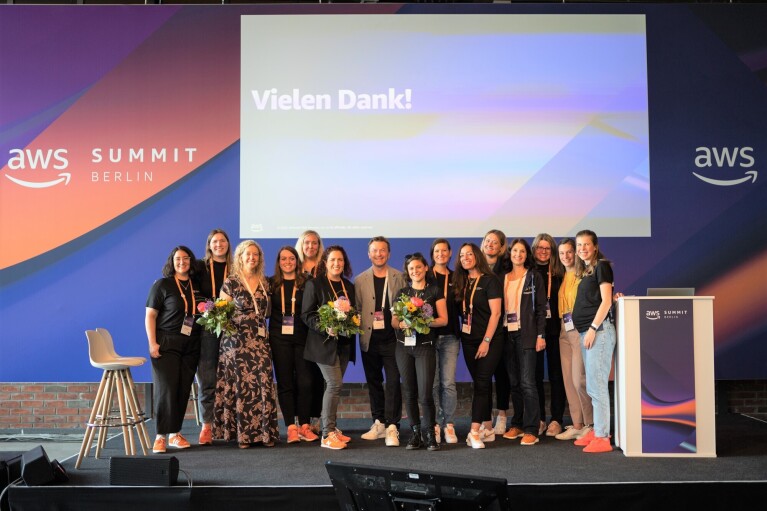 Gruppenbild von Klaus Bürg, Managing Director DACH bei AWS und dem GetIT Team aus Deutschland beim bedanken für die Präsentationen der Schulen auf dem AWS Summit in Berlin 2022. Die Gruppe steht auf einer Bühne und im Hintergrund ist "Vielen Dank" sowie "aws SUMMIT BERLIN" zu erkennen. Einige Frauen halten Blumensträuße.