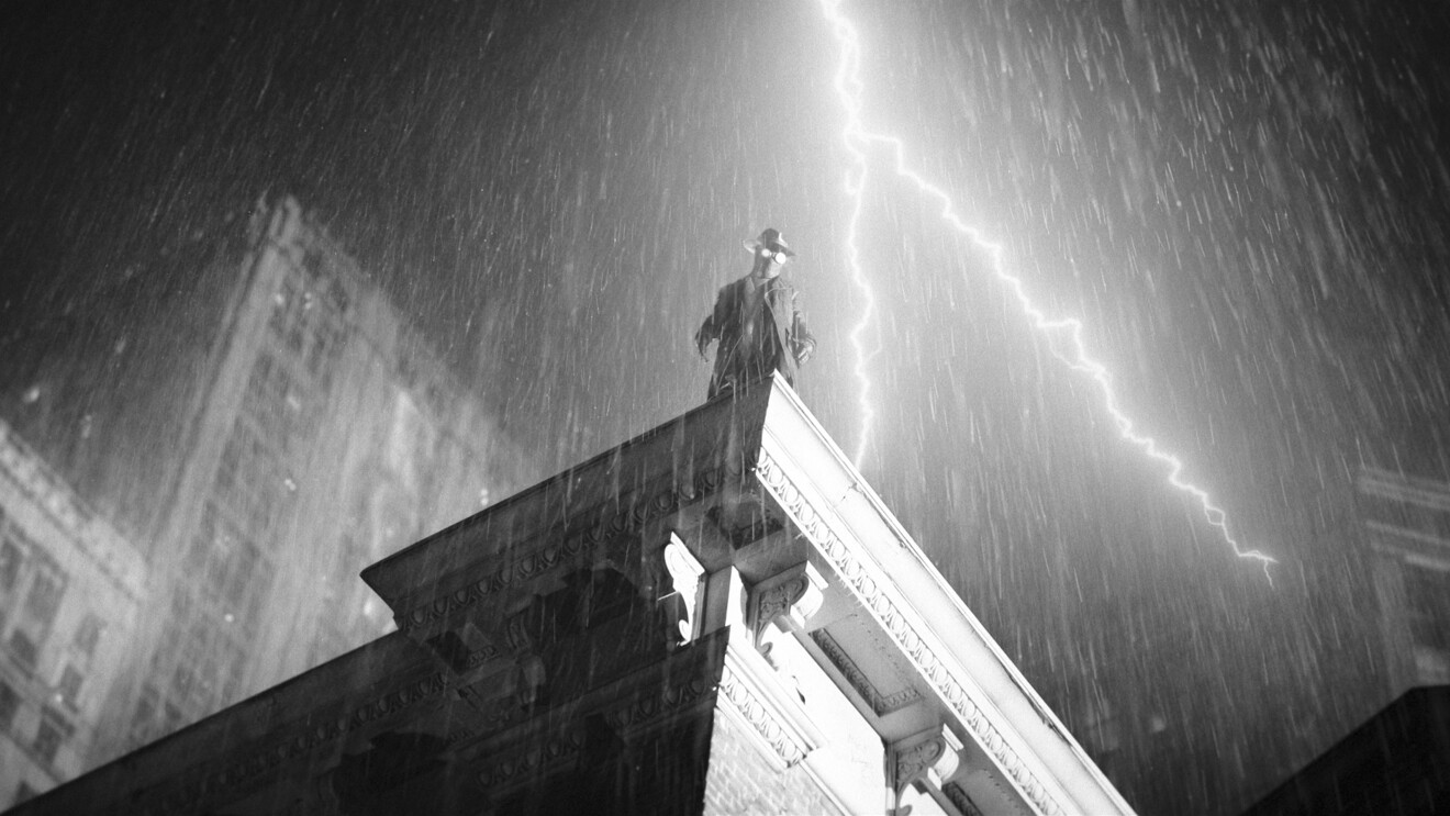 Silhouette of The Spider, played by Nicolas Cage, braving thunderstorm atop building