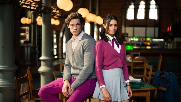 Man in gray sweater and woman in pink top standing in elegant hall with pendant lights