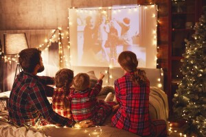 An image of a family sitting together watching a movie on a projector in a room decked out in holiday decorations