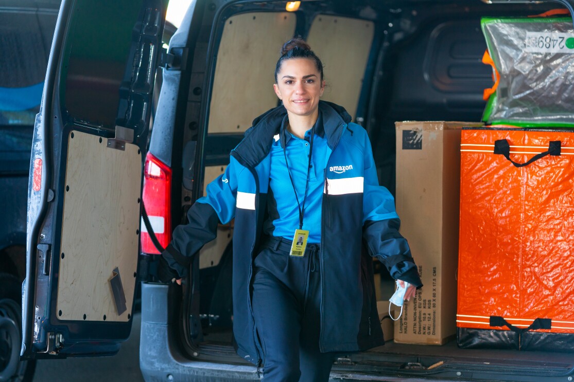 Eine junge Frau in Amazon Arbeitkleidung läuft vor einem Lieferwagen.