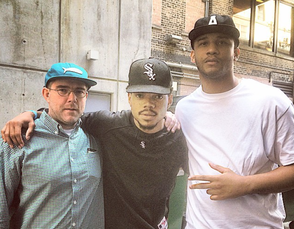 Three men stand for a photo in the alleyway of several brick buildings.