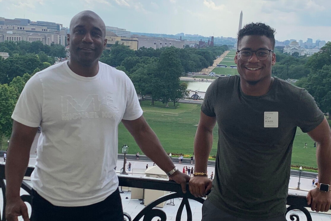 Jaren Kirkland stands next to his dad on a balcony with the Washington Monument behind them in the distance.