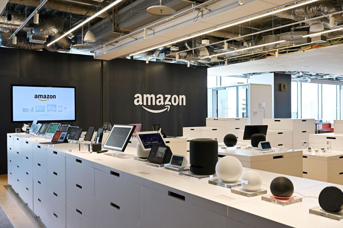 Amazon Echoなどの電化製品が棚の上に並べられている。その奥は黒い壁に白いAmazonのロゴとモニター