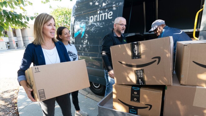一张四个人从亚马逊送货车上搬亚马逊盒子的图片。