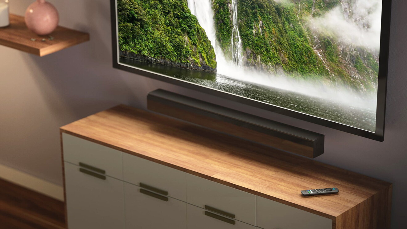 Fire TV Soundbar und Fernbedienung vor laufendem Fernseher mit Naturaufnahmen.