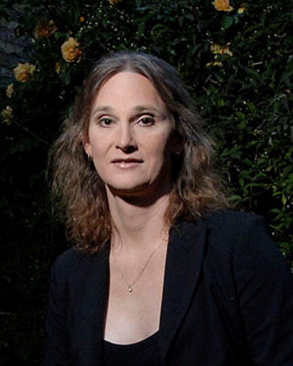 A headshot photo of Jessica Bussert smiling for a photo in front of a wall with greenery and yellow roses on it.