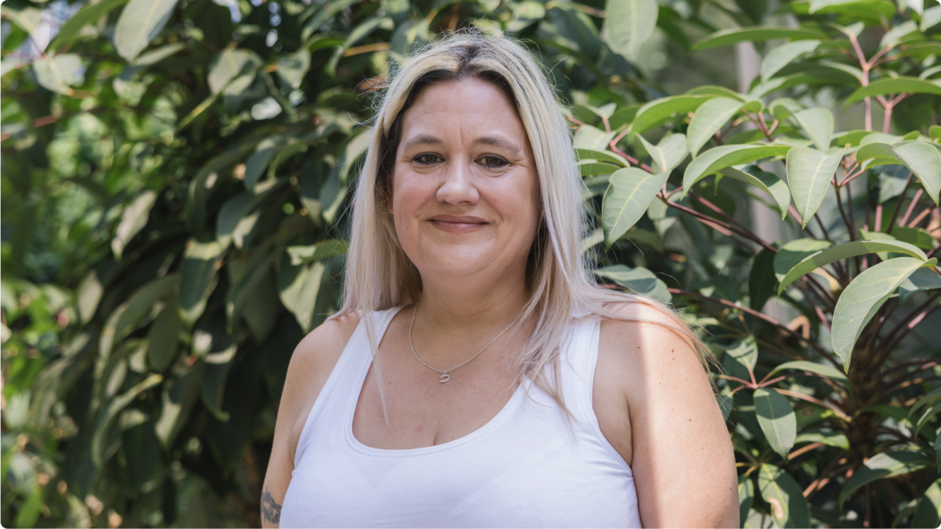 Blonde woman with friendly smile standing in front of foliage