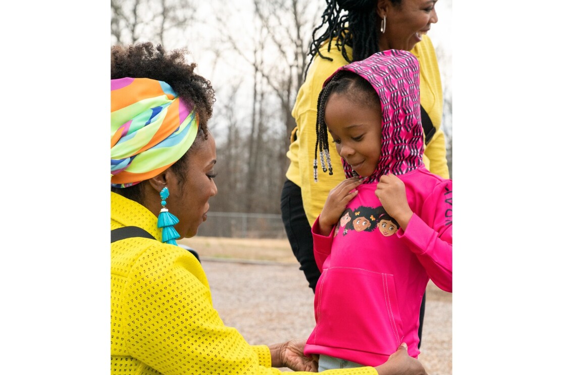 Cara and Jenae smile as they give children at a playground some of their apparel to wear.