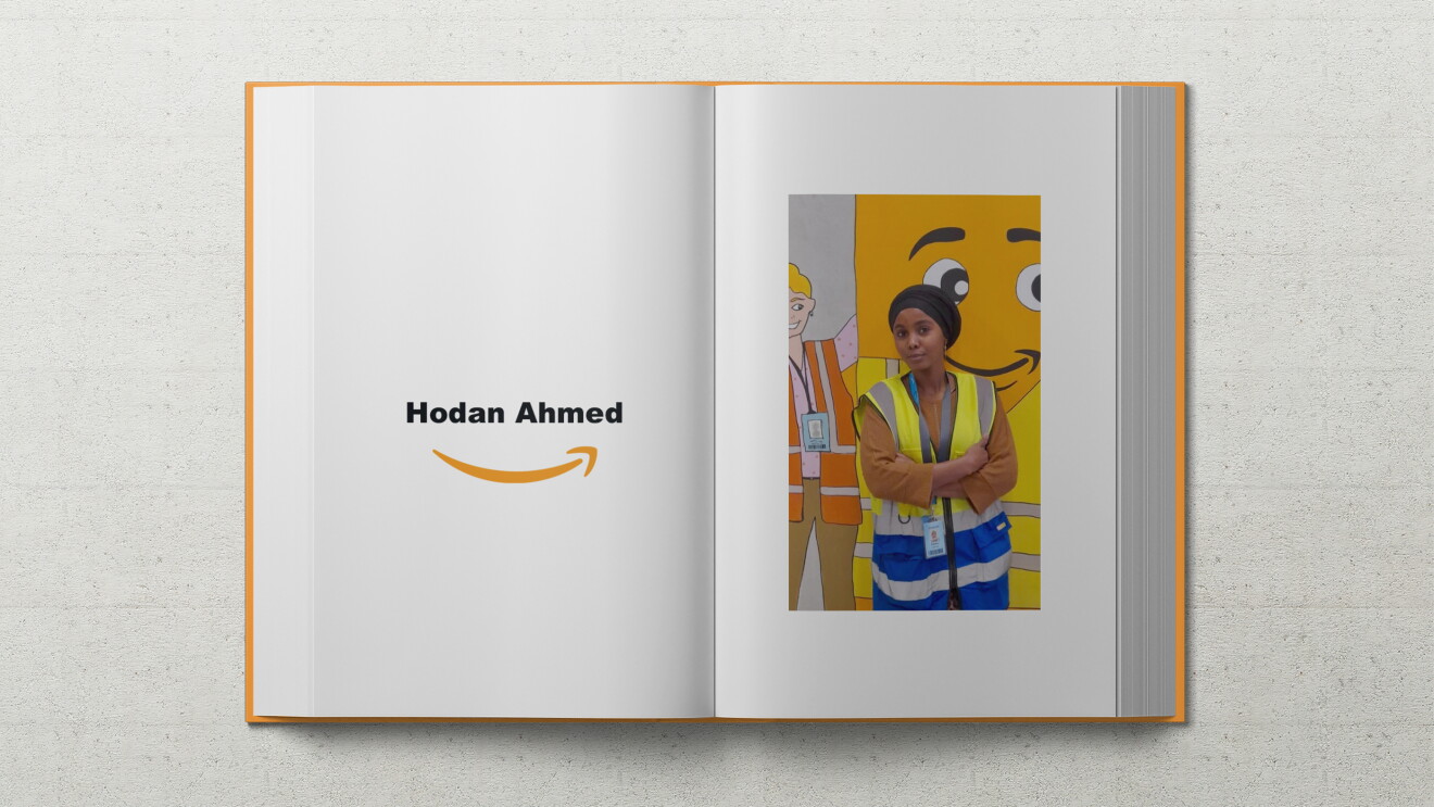 Hodan, eine junge Frau mit einem turbanartigen schwarzen Kopfschmuck, lehnt in Sicherheitsweste an einer Wand auf dem das Amazon Maskottchen Peccy abgebildet ist.