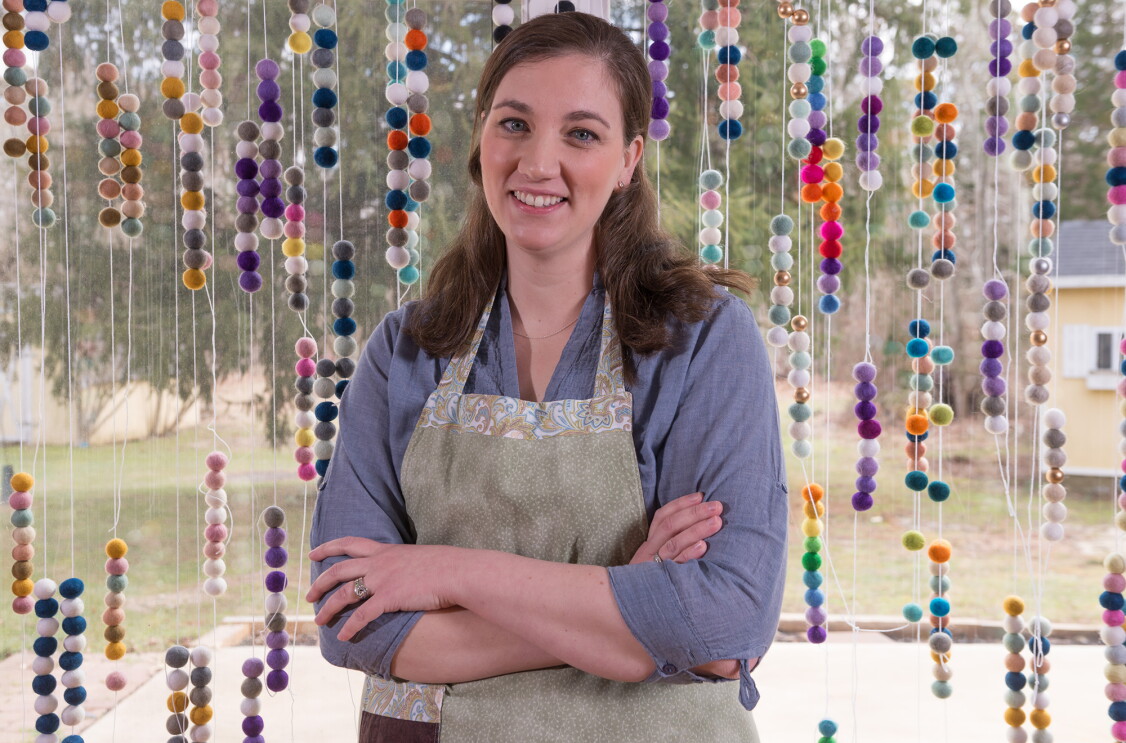 Amazon Handmade seller posing in a photograph in front of the felted wool ball garlands she makes and sells.