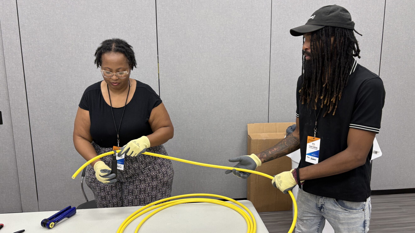 Two workers in protective gloves handling yellow cable or tubing