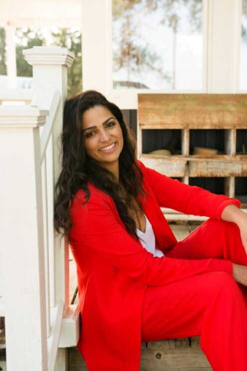 Camila Alves McConaughey wears a red suit and sits on the floor next to a white stair rail