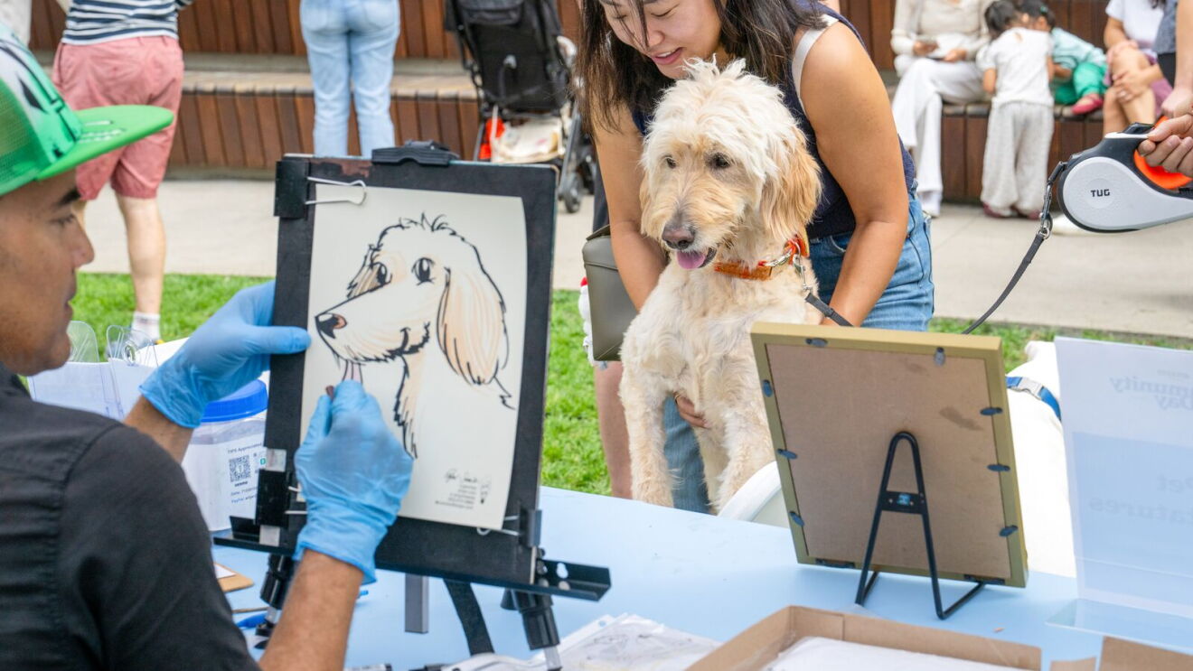 Dog posing with owner as caricaturist draws its picture