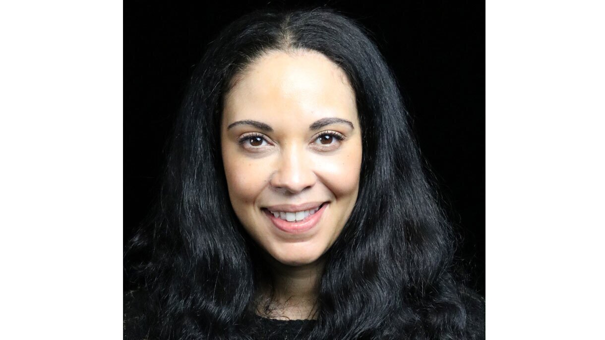 A headshot image of a woman smiling for the photo in front of a black background.