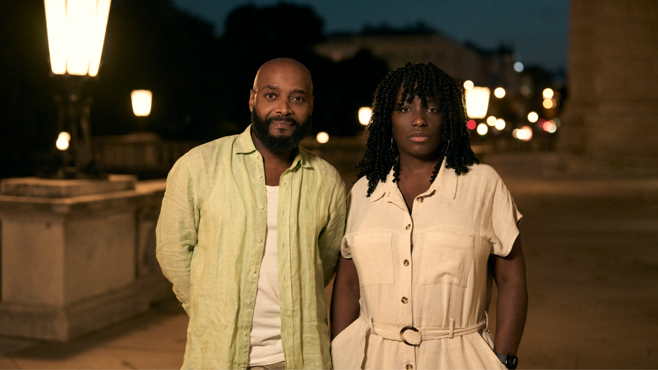A stylish couple looking towards the camera on a dimly lit London street