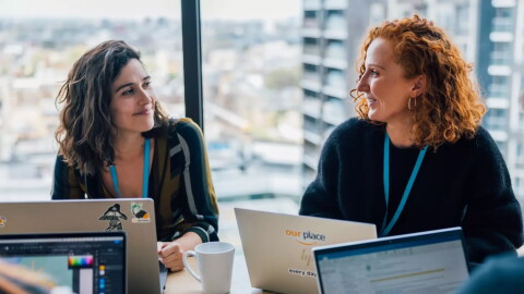 Two women sitting at a desk in front of laptops