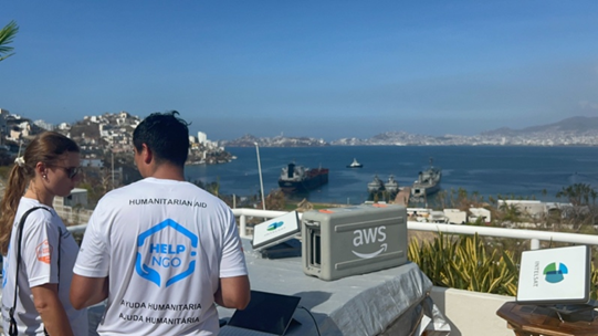 Dos personas con la camiseta de Help NGO y unos dispositivos de AWS en la bahía de Acapulco. 