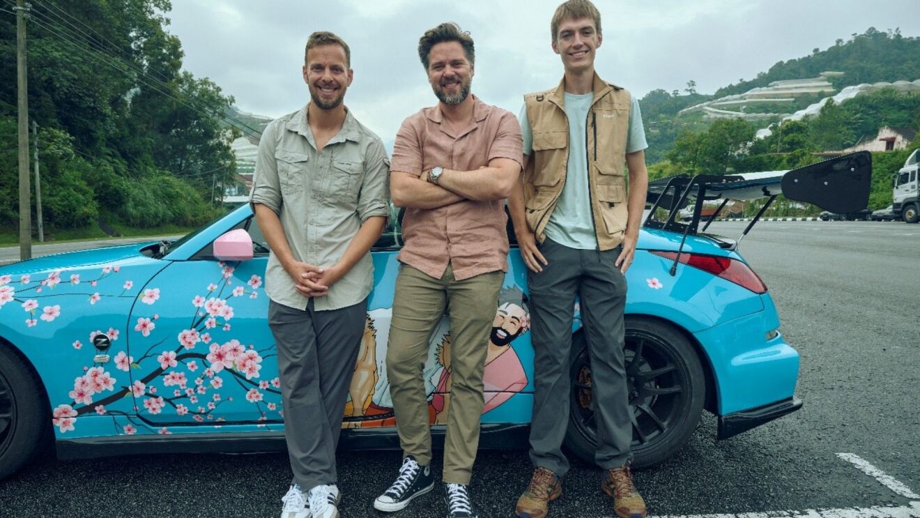 Three men standing by a blue car