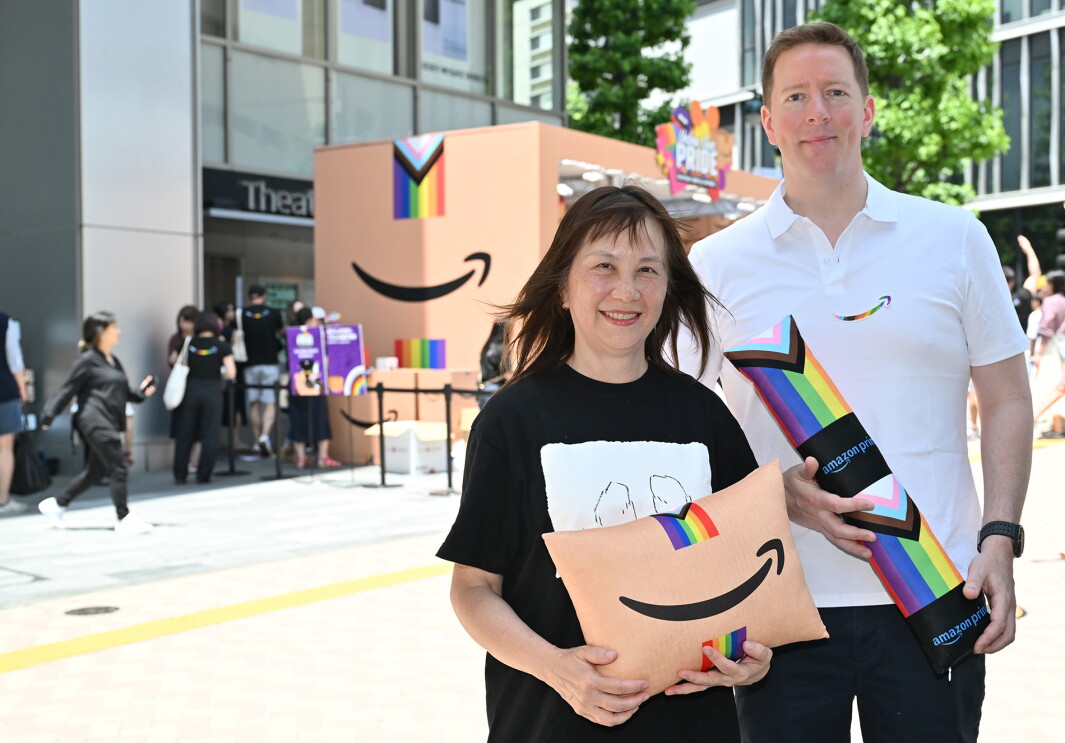 ブースの前に立つ黒いTシャツを着た女性と白いポロシャツを着た男性。それぞれ手にはAmazonのロゴが入ったクッションを持っている