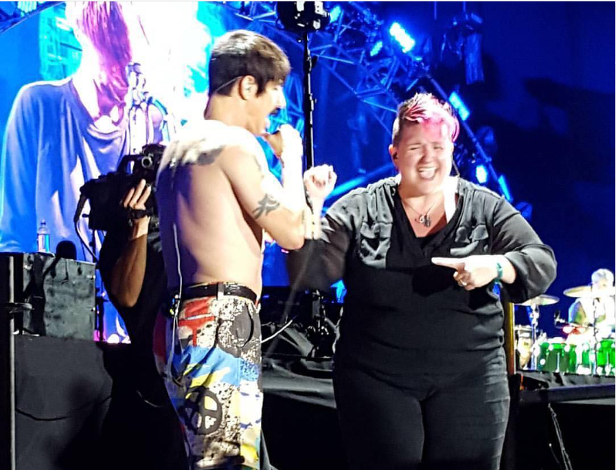 An image of Amber Galloway-Gallego on stage signing while Anthony Kiedis sings during a Red Hot Chili Peppers concert.