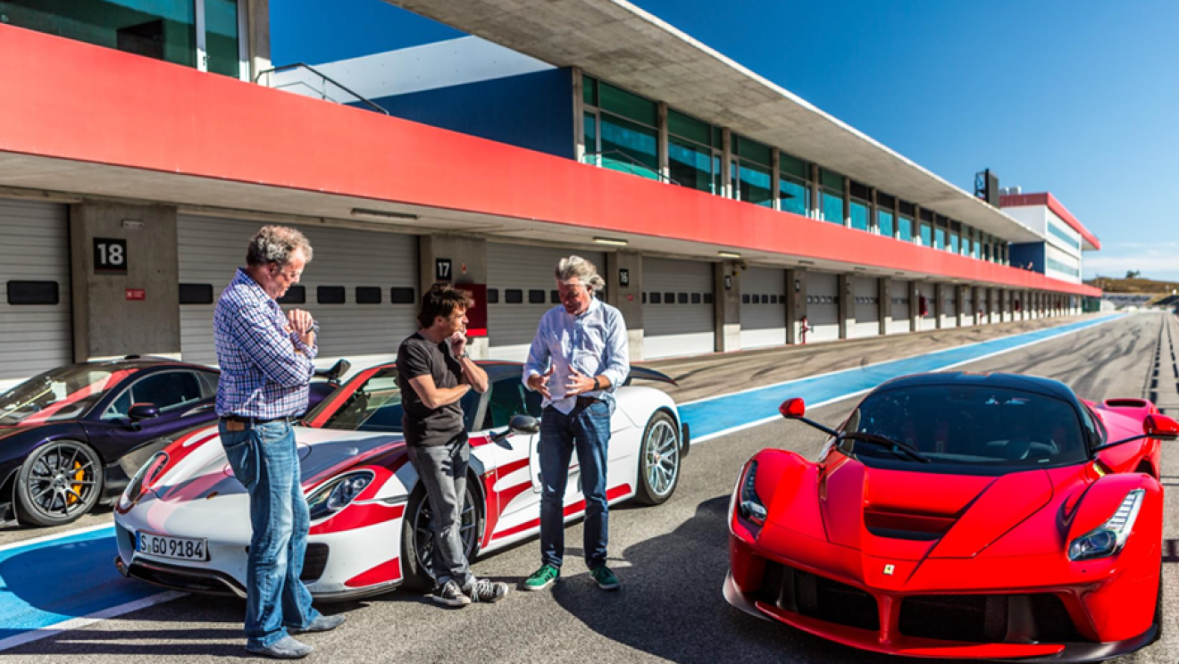 Jeremy Clarkson, Richard Hammond and James May stand next to three sports cars on a race track