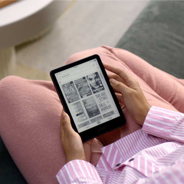 Woman on a sofa holding a Kindle showing a selection of book covers