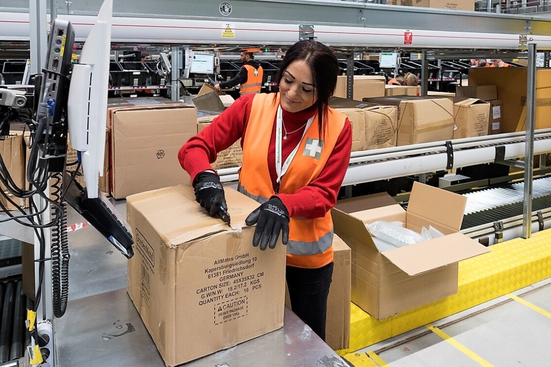 Eine Mitarbeiter, die Sicherheitshandschuhe trägt, öffnet mit einem Cutter eine Kartonage.