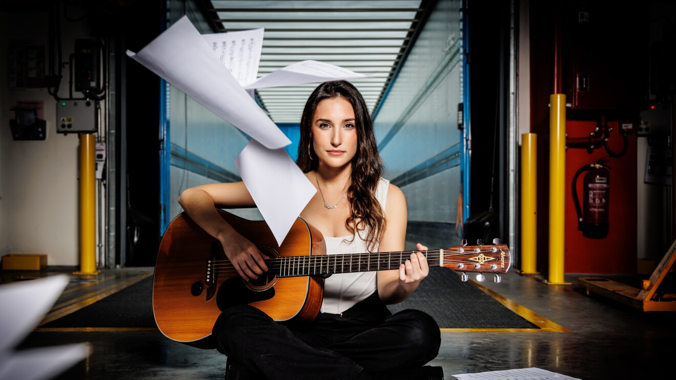 Con el remolque de un camión abierto y vació, justo en la entrada aparece Marta con el pelo ondulado suelto, jersey blanco sin mangas y un pantalón negro tocando una guitarra española. Por el suelo está lleno de partituras y también hay cuatro hojas de partituras sobrevolando su cabeza.   