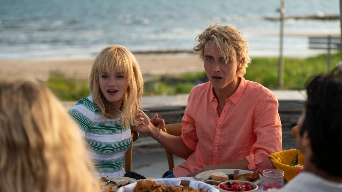 A scene from We Were Liars with blonde woman and man in pink shirt with surprised look at outdoor meal