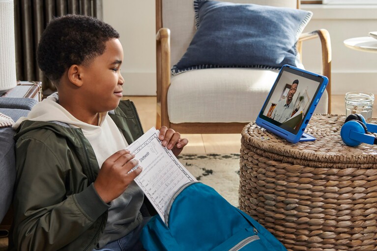 A boy engages with a man on a fire tablet, while pulling homework from a backpack.