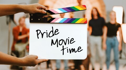 Movie clapboard decorated with Pride colours with a blurry figures in the background