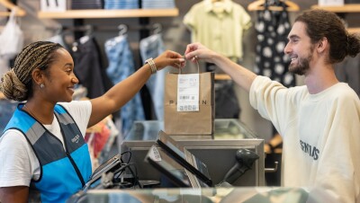 亚马逊员工穿着一件蓝色的亚马逊背心,她抓住一个零售袋从PacSun柜台员工的另一面。