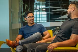 An image of two men seated in chairs talking in an office setting.