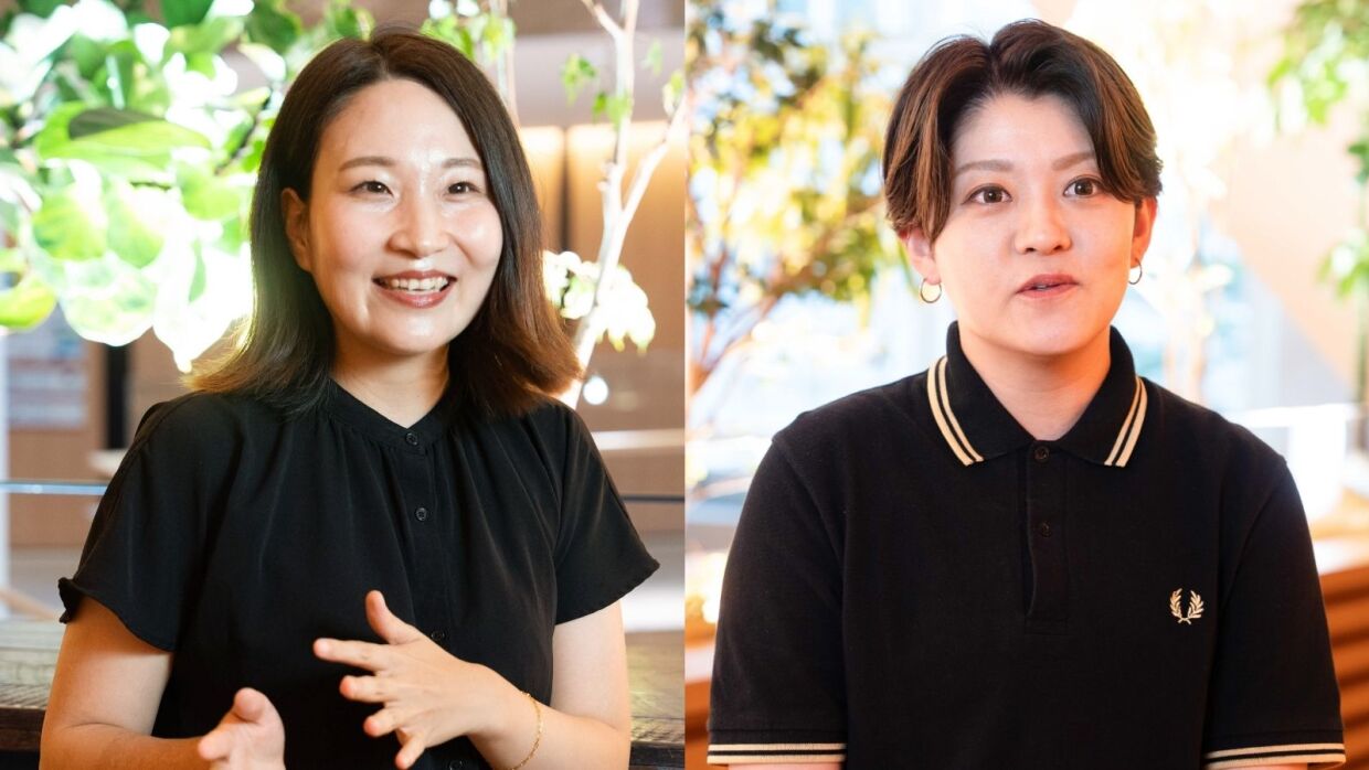 左には黒いブラウスを着ている女性が手を広げて説明するように話している。右側には黒いポロシャツを着たショートヘアの女性が話をしている