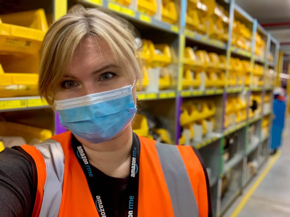 Natalya-Selfie: Sie trägt Maske und Sicherheitsweste. Im Hintergrund sind man Regal mit gelben Materialboxen.
