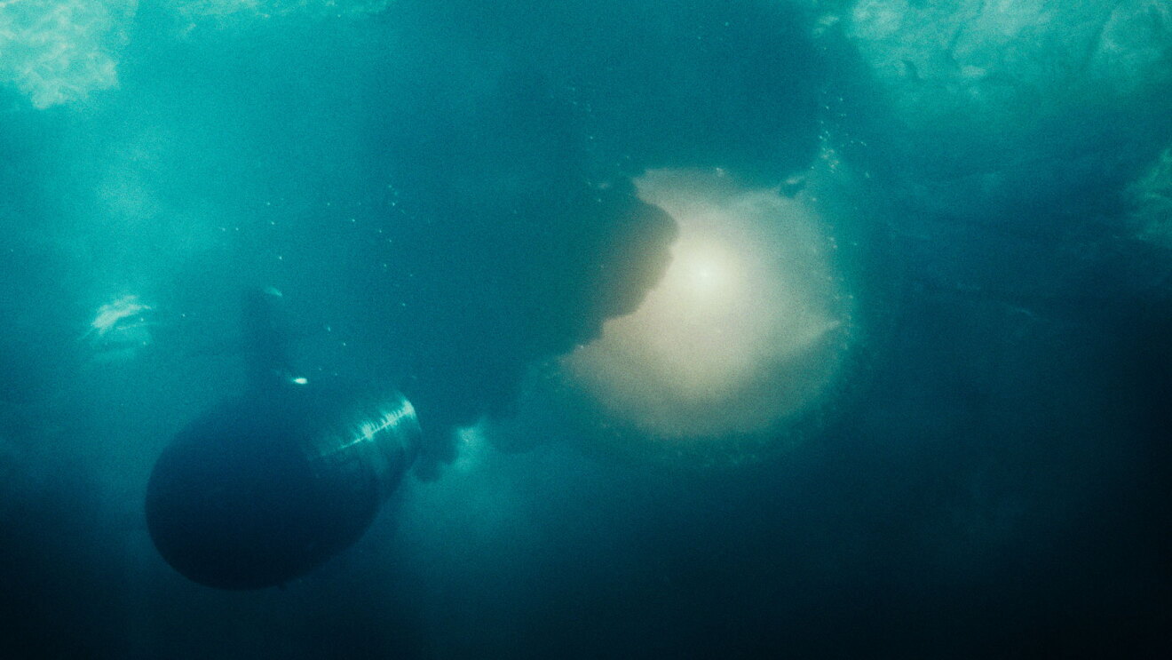 海の中を進む潜水艦が、爆発をよけている。潜水艦の後ろには黒い煙があがり、光や水の泡が見える。