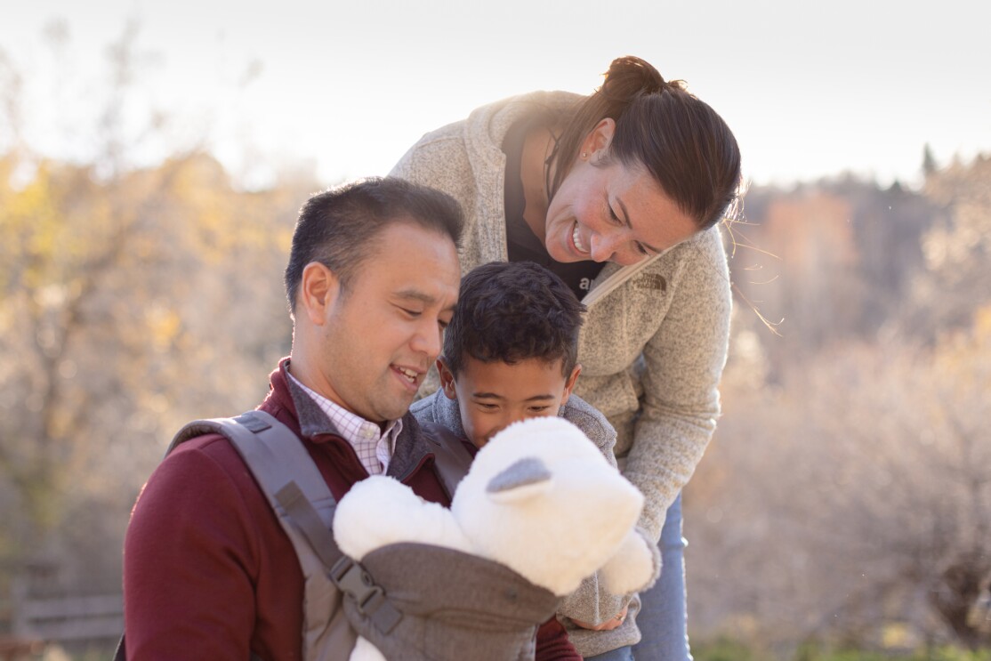 A man, woman, and child all look at an infant in a baby carrier.