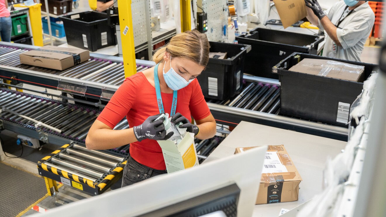 L'immagine mostra una donna dipendente amazon all'interno del magazzino che ispeziona  i prodotti resi e li valuta